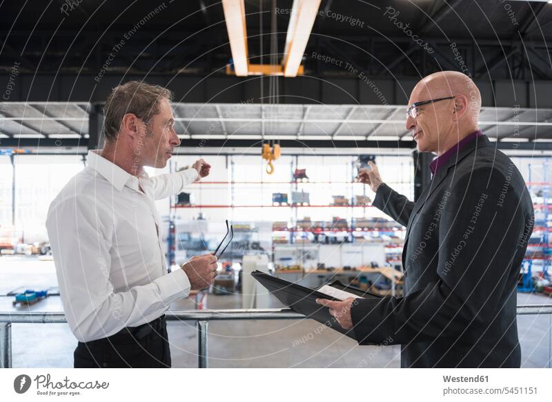 Two businessmen with clipboard talking on factory shop floor Businessman Business man Businessmen Business men factories business people businesspeople