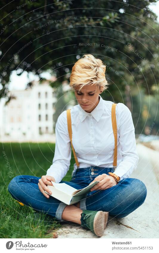 Teenage girl sitting cross-legged in a park, reading book tailor seat Seated hip trendy learning books blond blond hair blonde hair Teenage Girls
