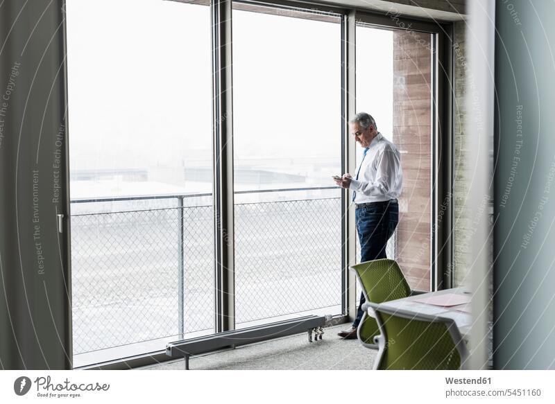 Senior manager in office standing at the window holding smartphone message Smartphone iPhone Smartphones Businessman Business man Businessmen Business men