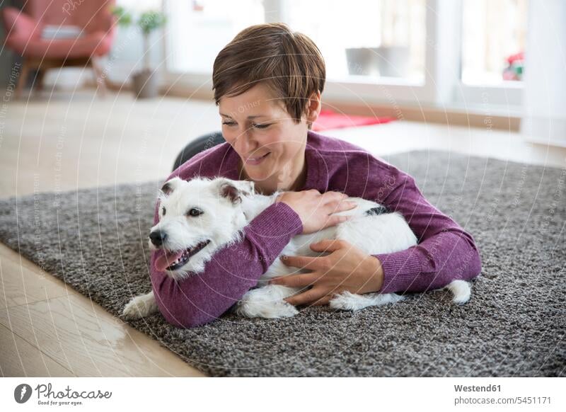 Woman lying on carpet in the living room hugging her dog dogs Canine woman females women pets animal creatures animals Adults grown-ups grownups adult people