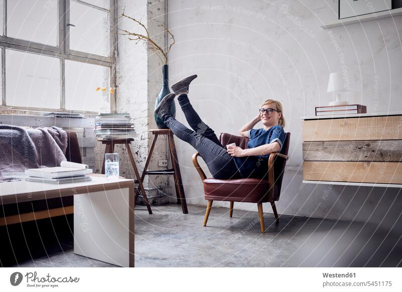 Happy woman sitting with legs in the air on armchair in loft lofts freelancer freelancing females women Adults grown-ups grownups adult people persons
