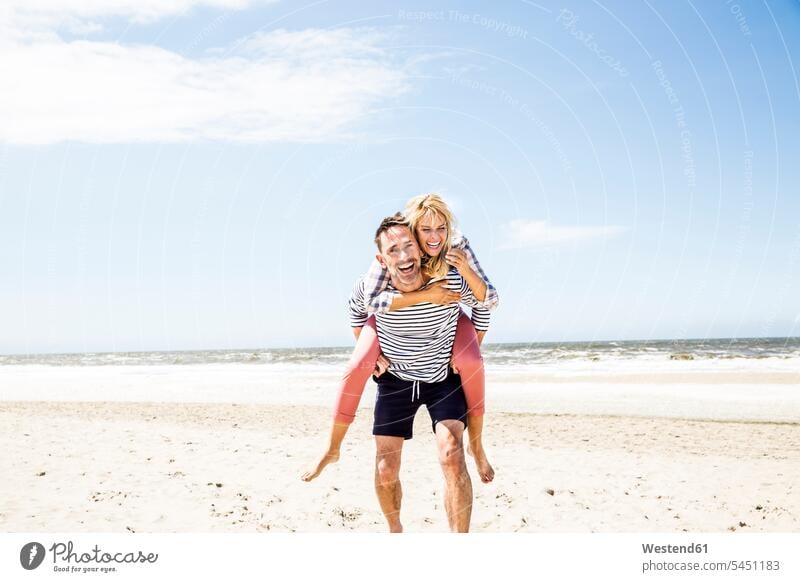 Happy playful couple on the beach laughing Laughter piggyback piggy-back pickaback Piggybacking Piggy Back beaches twosomes partnership couples positive Emotion