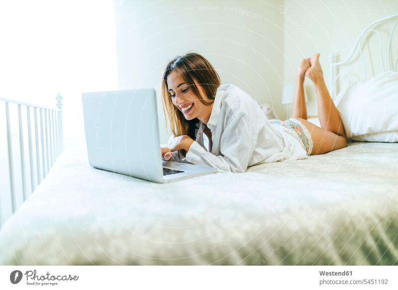 Smiling woman lying on the bed using a laptop beds Laptop Computers laptops notebook females women computer computers Adults grown-ups grownups adult people