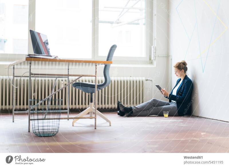 Businesswoman sitting on floor in office using digital tablet Seated working At Work offices office room office rooms Internet The Internet businesswoman