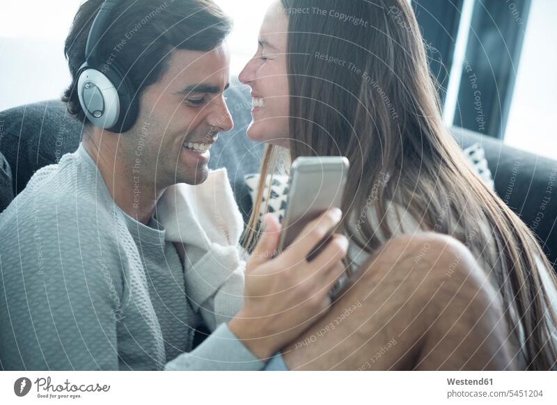 Happy young couple with headphones and smartphone at home twosomes partnership couples relaxed relaxation headset happiness happy people persons human being