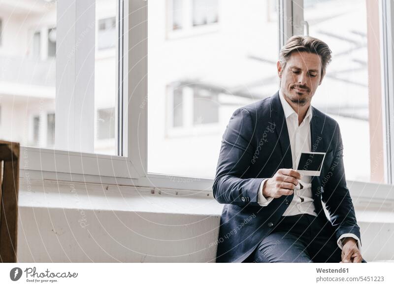 Businessman at the window looking at instant photo photograph photographs photos serious earnest Seriousness austere Business man Businessmen Business men image