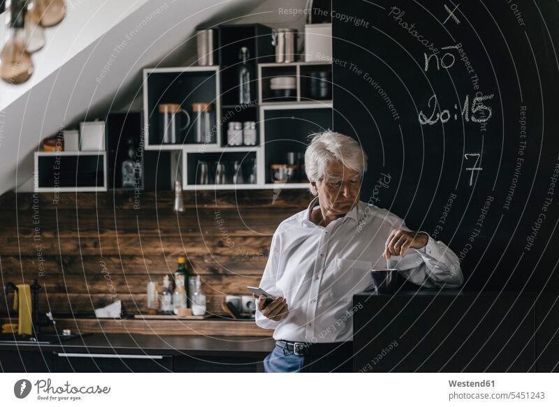 Senior businessman with smartphone and cup of coffee in the kitchen domestic kitchen kitchens senior men senior man elder man elder men senior citizen Coffee