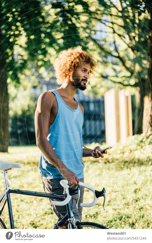 Young man with bicycle and cell phone in park bikes bicycles men males mobile phone mobiles mobile phones Cellphone cell phones Adults grown-ups grownups adult