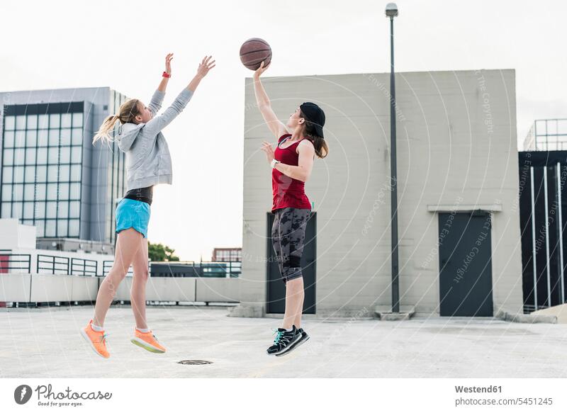 Two women playing basketball on parking level in the city woman females female friends basketballs Adults grown-ups grownups adult people persons human being