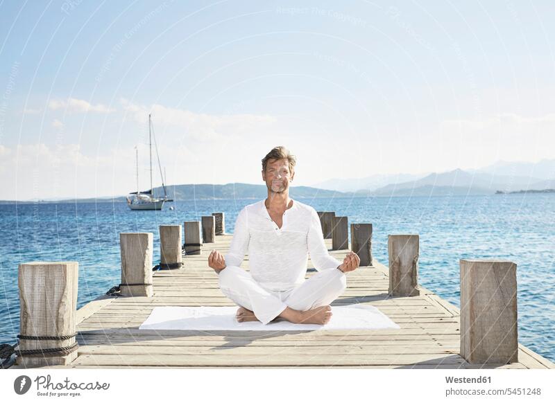 Mature man doing yoga exercise on jetty men males mindfulness aware awareness self-care relaxation exercise relaxed relaxing Adults grown-ups grownups adult