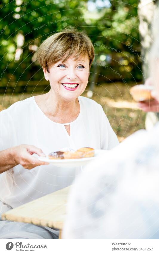 Smiling senior woman offering muffins senior women elder women elder woman old females smiling smile senior adults Adults grown-ups grownups people persons