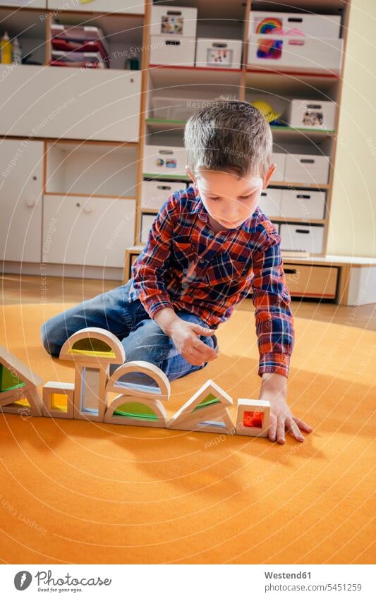 Boy lining up wooden toy shapes on carpet in kindergarten child children kid kids boy boys males nursery school playing people persons human being humans