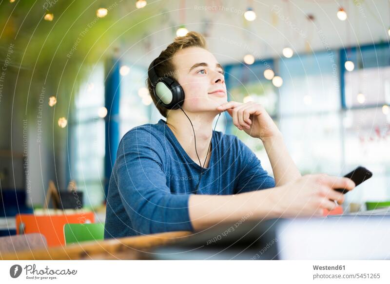 Portrait of young man listening music with headphones in a coffee shop headset student students portrait portraits cafe hearing men males Adults grown-ups