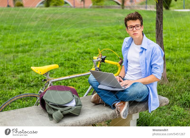 Pensive young man with racing cycle sitting on a bench using laptop men males Laptop Computers laptops notebook Adults grown-ups grownups adult people persons