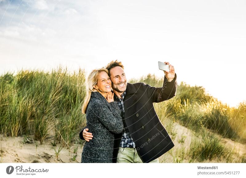 Happy couple in dunes taking a selfie twosomes partnership couples beach beaches Selfie Selfies mobile phone mobiles mobile phones Cellphone cell phone