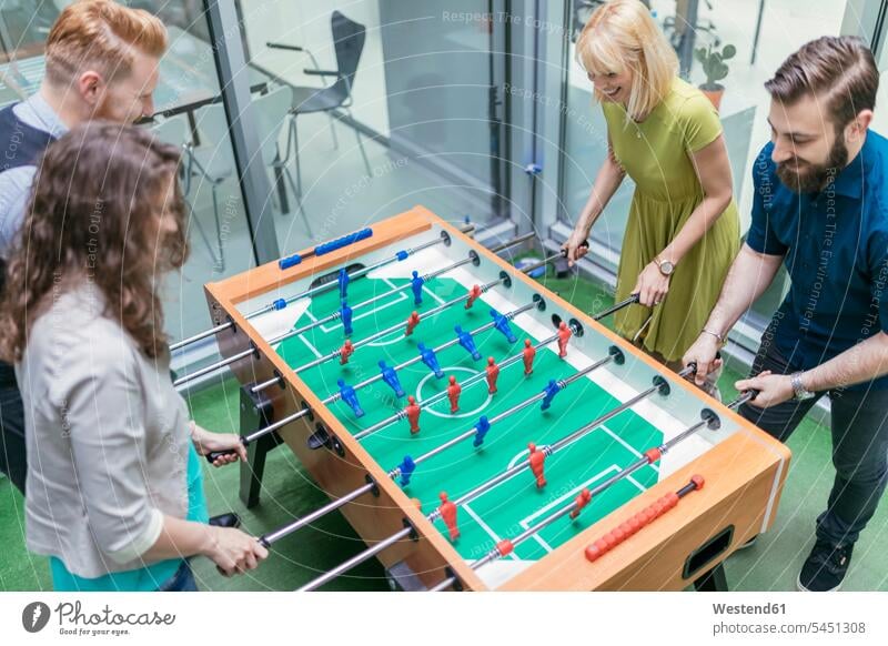 Colleagues playing foosball in office together table football table soccer business people businesspeople offices office room office rooms business world