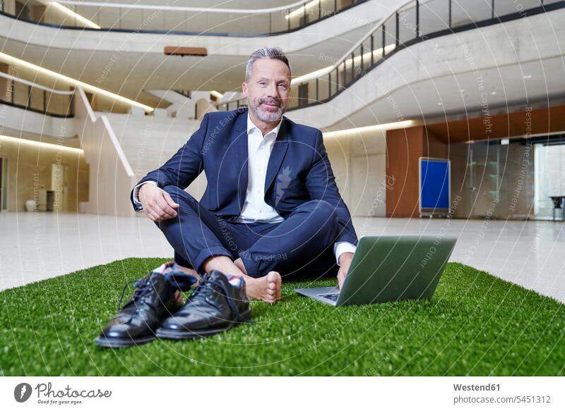 Businesssman sitting on synthetic turf using laptop Laptop Computers laptops notebook smiling smile Businessman Business man Businessmen Business men Seated