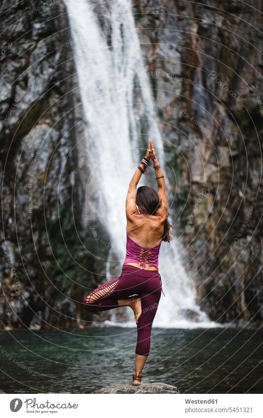 Italy, Lecco, woman doing Tree Yoga Pose on a rock near a waterfall waterfalls yoga females women standing waters body of water mindfulness aware awareness