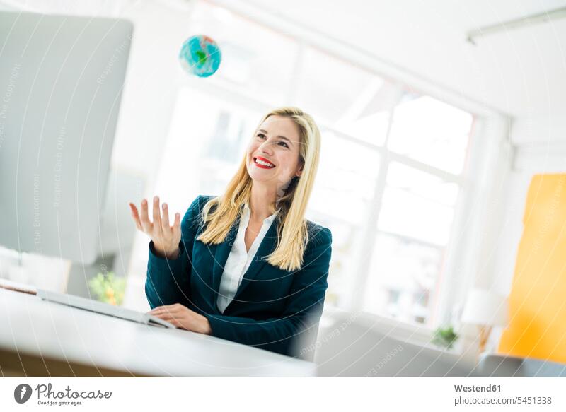 Smiling businesswoman at desk throwing up mini globe smiling smile Office Offices globes businesswomen business woman business women business people