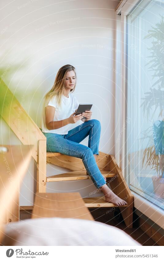 Young woman sitting at home using digital tablet stairs stairway reading Seated cozy sociable comfortable cosy females women Planning planning planned digitizer