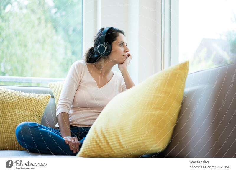 Woman sitting alone on couch, listening music with headphones Listening Music Seated solitary solo headset settee sofa sofas couches settees copy space