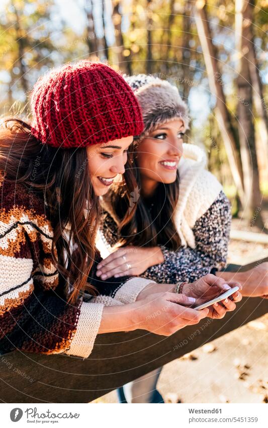 Two pretty women using smartphone in an autumnal forest woman females use female friends Smartphone iPhone Smartphones beautiful woods forests fall Adults