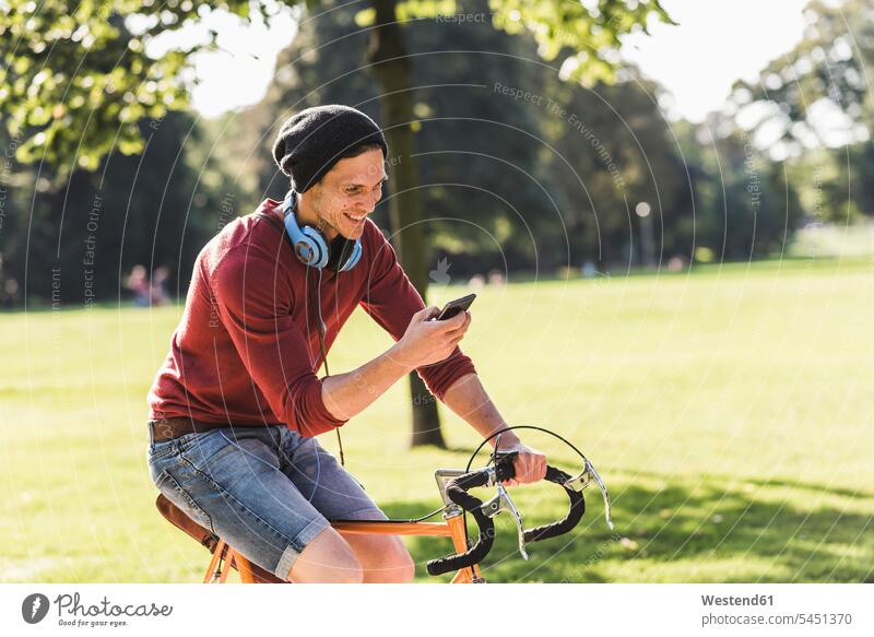 Laughing man on racing cycle looking at cell phone in a park bicycle bikes bicycles parks men males Adults grown-ups grownups adult people persons human being