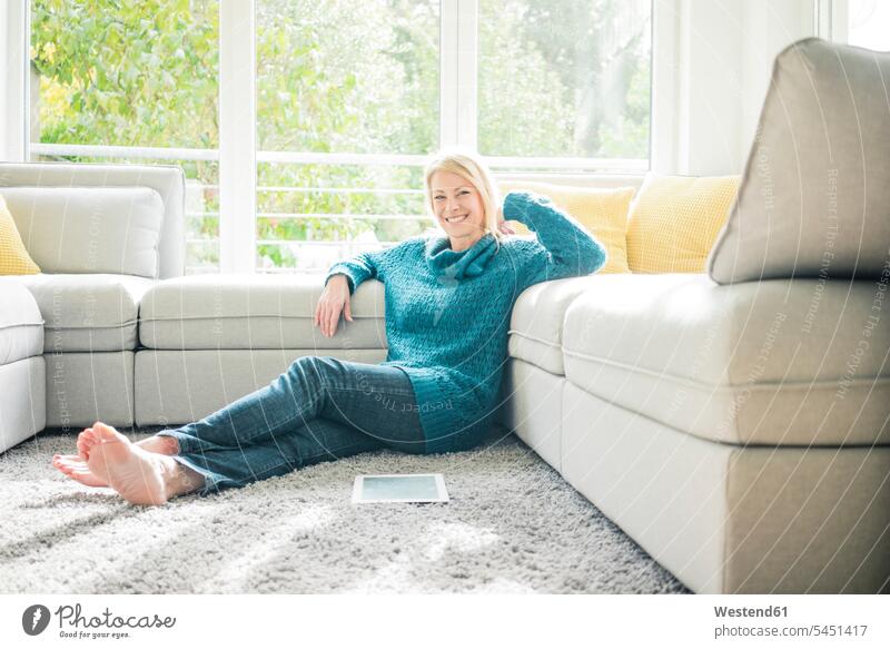 Portrait of smiling woman relaxing in living room living rooms livingroom portrait portraits sitting Seated smile females women tablet digitizer Tablet Computer