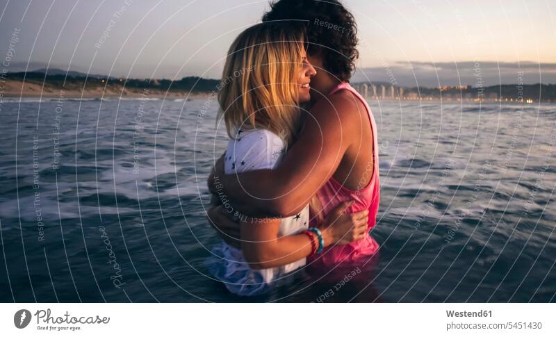 Young couple hugging in the sea at dusk ocean smiling smile embracing embrace Embracement twosomes partnership couples water waters body of water people persons