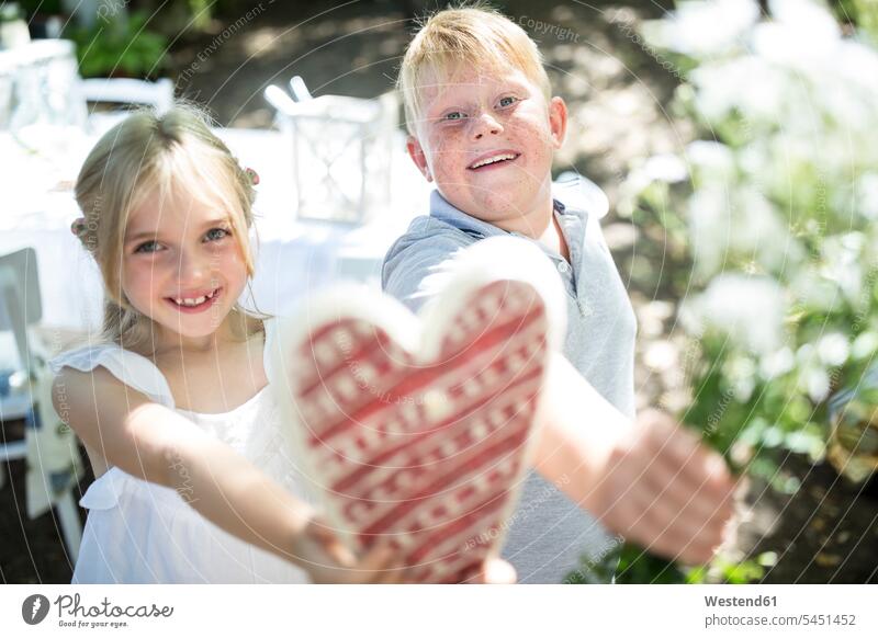 Smiling sister and brother holding heart and bunch of flowers sisters brothers smiling smile Mother's Day mothers day siblings brother and sister