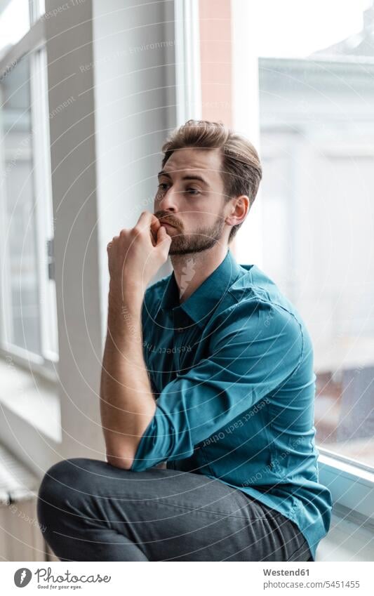 Portrait of pensive young man sitting on window sill men males Adults grown-ups grownups adult people persons human being humans human beings serious earnest