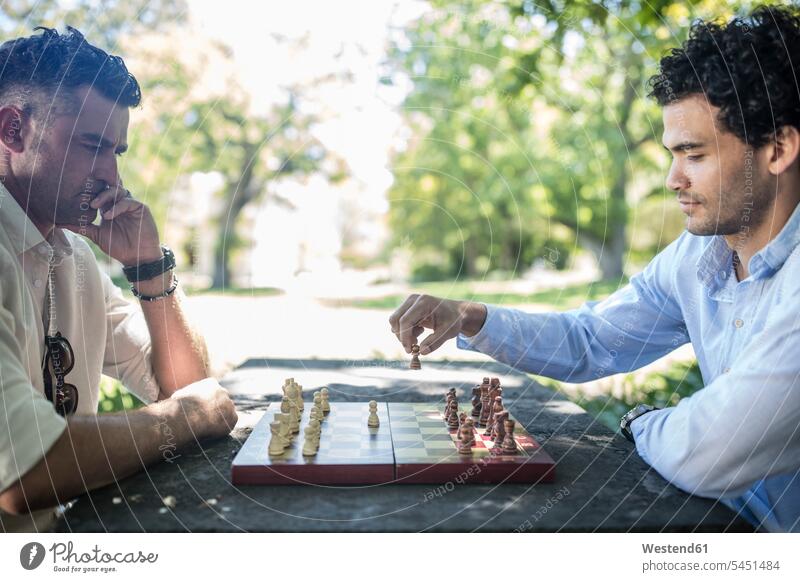 Two men playing game of chess in park man males board game board-games boardgame board games parlor game parlour games parlor games Adults grown-ups grownups
