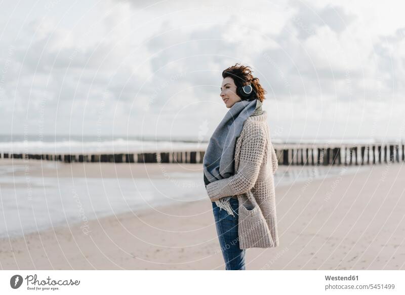 Woman standing on the beach with headphones woman females women headset hearing beaches Adults grown-ups grownups adult people persons human being humans
