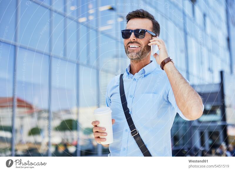 Cheerful businessman talking on phone and holding coffee outdoors smiling smile Coffee on the phone call telephoning On The Telephone calling mobile phone