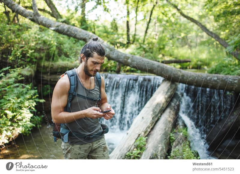 Young man holding cell phone at a waterfall in forest mobile phone mobiles mobile phones Cellphone cell phones hiker wanderers hikers hiking men males