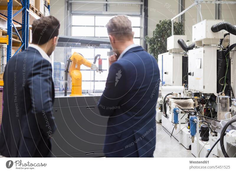 Two businessmen in factory shop floor looking at industrial robot colleagues man males factories eyeing Adults grown-ups grownups adult people persons
