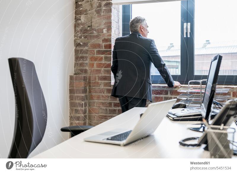 Mature businessman standing in office, looking out of window, rear view decision deciding decide decisions Responsibility responsible businesswear