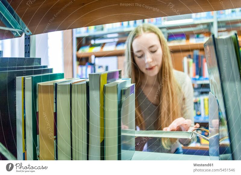 Teenage girl behind bookshelf in a public library Teenage Girls female teenagers reader readers reading Teenager Teens people persons human being humans