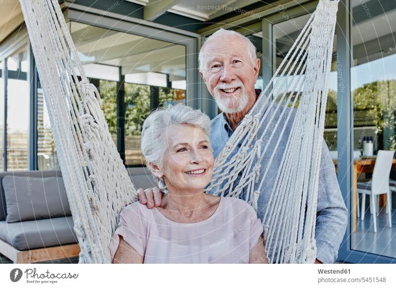 Senior couple on terrace, woman sitting in hammock twosomes partnership couples Aging Ageing Seated together happiness happy terraces senior adults seniors old