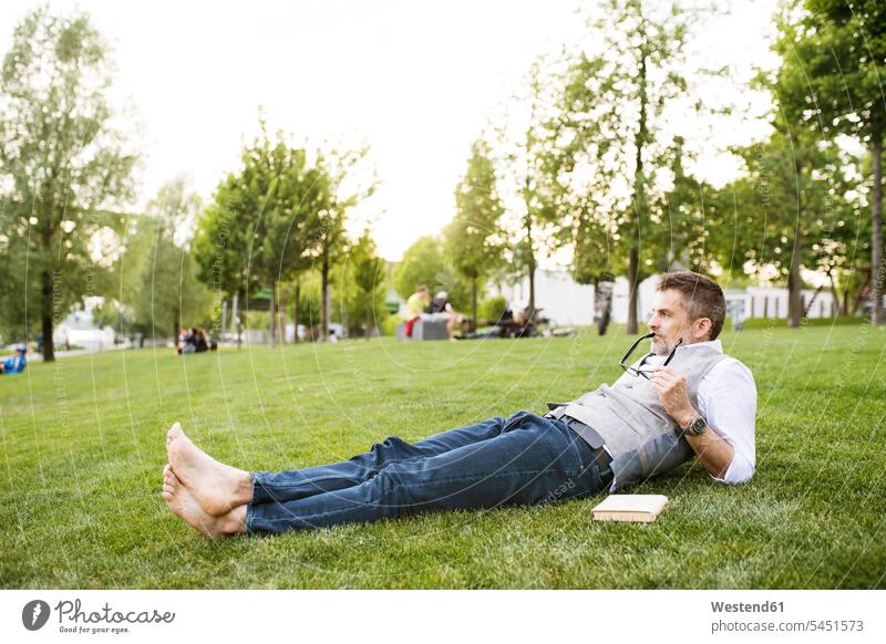 Mature businessman in the city park lying on grass laying down lie lying down meadow meadows relaxed relaxation men males break relaxing Adults grown-ups
