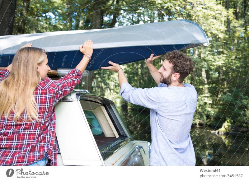 Smiling young couple taking canoe from car roof forest woods forests twosomes partnership couples take smiling smile automobile Auto cars motorcars Automobiles