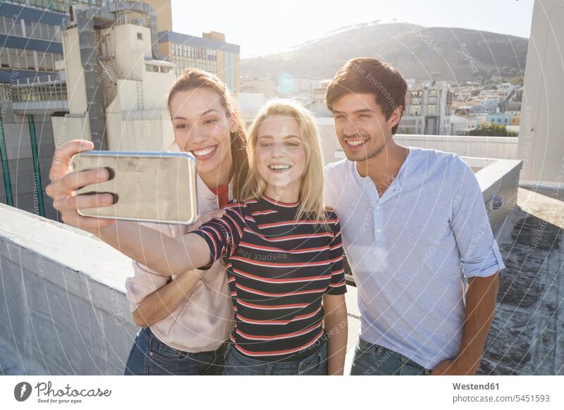 Friends taking selfies on a rooftop terrace camera cameras Selfie Selfies photographing celebrating celebrate partying roof terrace deck smiling smile friends
