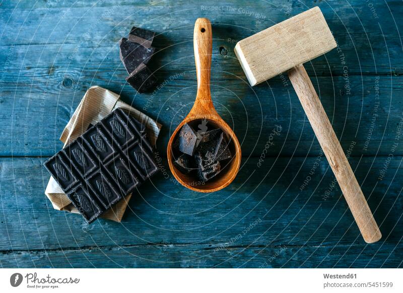 Dark chocolate on paper, wooden spoon and wooden hammer on blue wood crushed crushing Series Part of A Series pieces chocolate bar chocolate bars