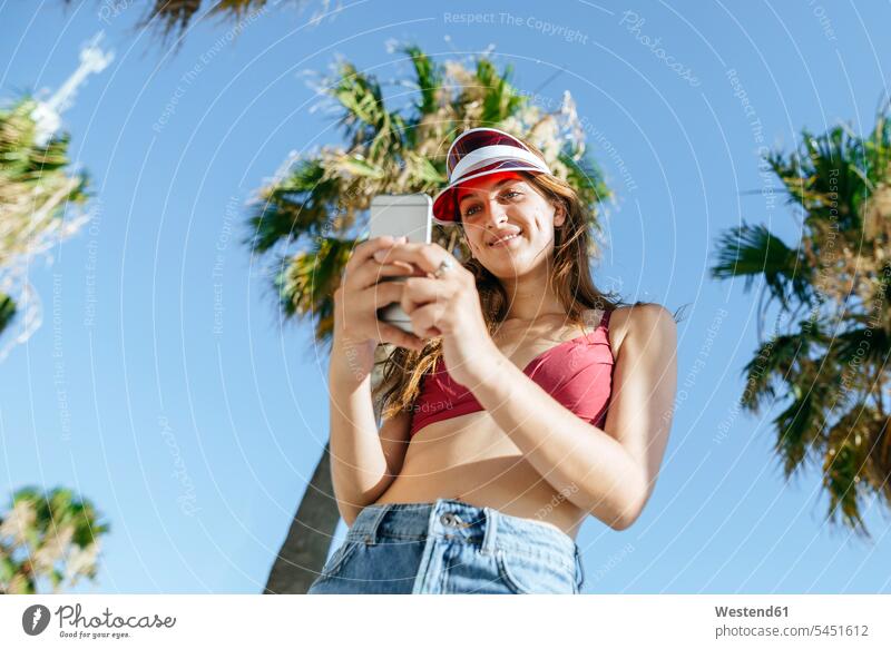Young woman with sun visor and bikini using cell phone standing smiling smile mobile phone mobiles mobile phones Cellphone cell phones females women telephones