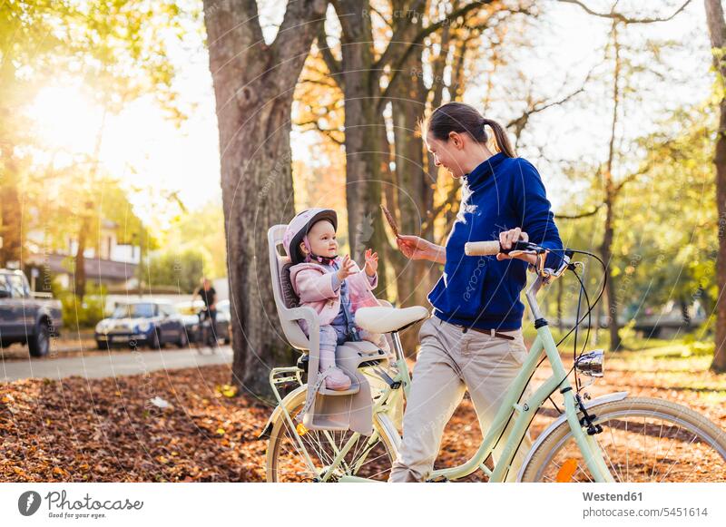 Mother and daughter riding bicycle, baby wearing helmet sitting in children's seat bikes bicycles playing Child's Seat child seat child safety seat riding bike