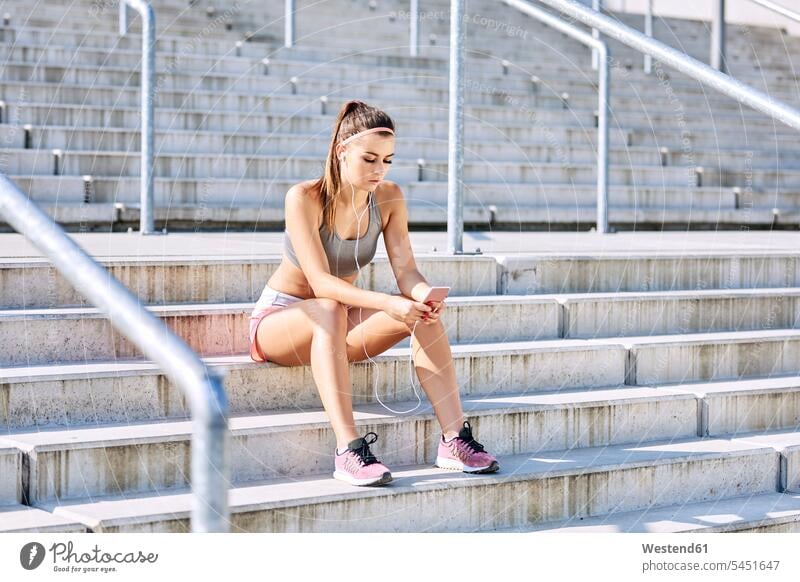 Fit woman sitting on stairs with smartphone and earphones ear phone ear phones mobile phone mobiles mobile phones Cellphone cell phone cell phones Smartphone
