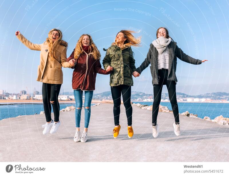 Four friends holding hands jumping in the air mate female friend jumps Leaping Emotions Feeling Feelings Sentiment Sentiments laugh Laughter portraits human
