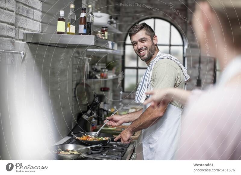 Smiling man preparing meal looking at wife cooking couple twosomes partnership couples smiling smile people persons human being humans human beings caucasian