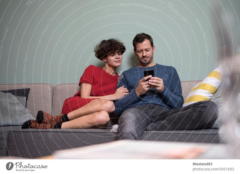 Couple sitting together on the couch looking at cell phone settee sofa sofas couches settees Smartphone iPhone Smartphones couple twosomes partnership couples