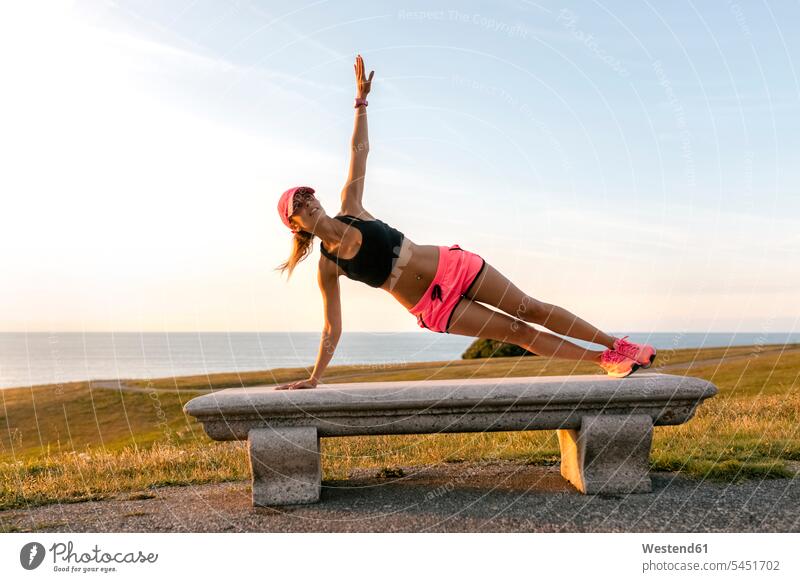 Young woman doing strength training on a bench at the sea fit exercising exercise practising warming up warm up females women side plank side planks Strength